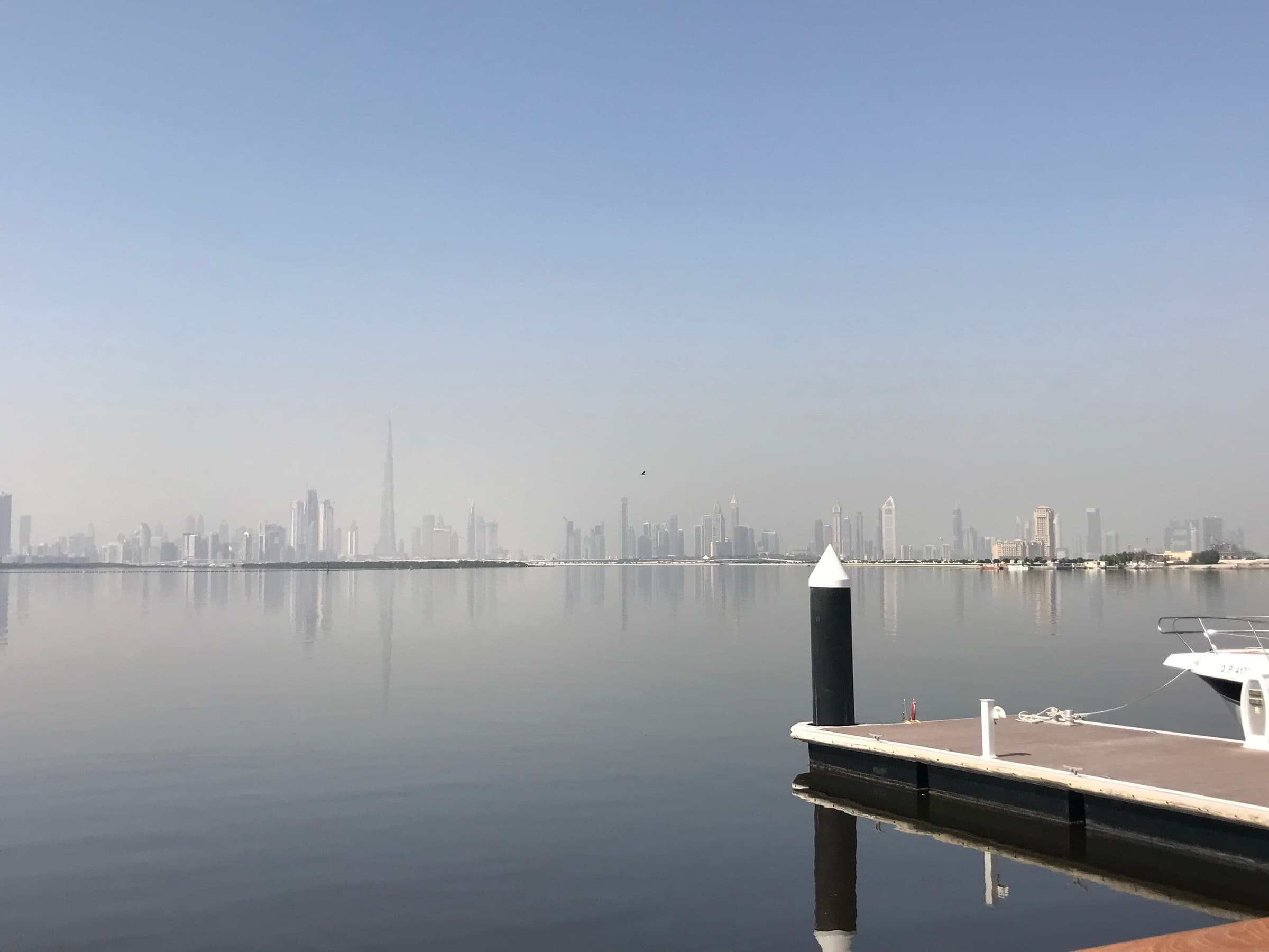 Calm morning view across the water from Dubai Creek Harbour toward the distant Dubai skyline and Burj Khalifa
